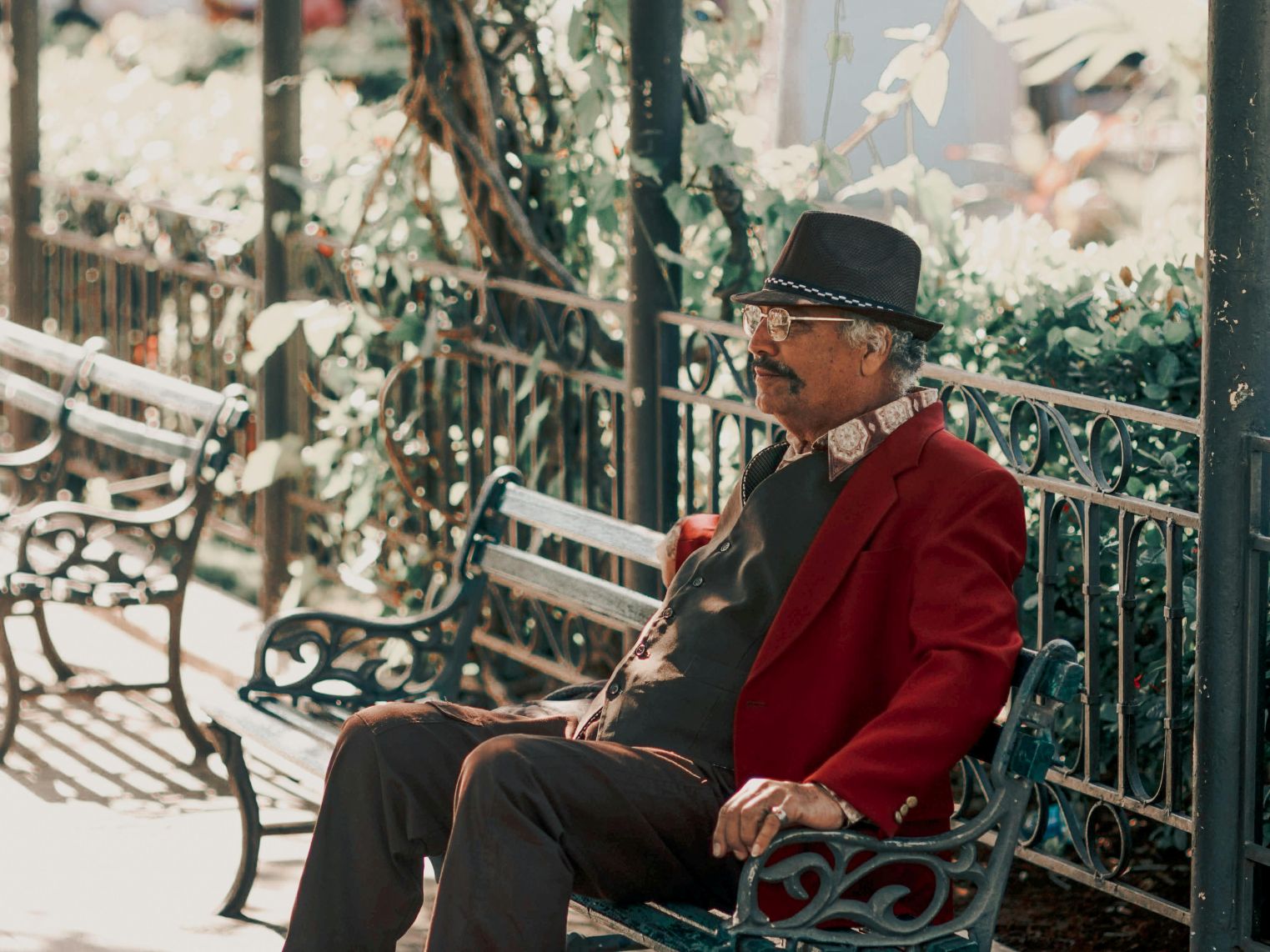Senior man sits on bench outdoors at bus stop.